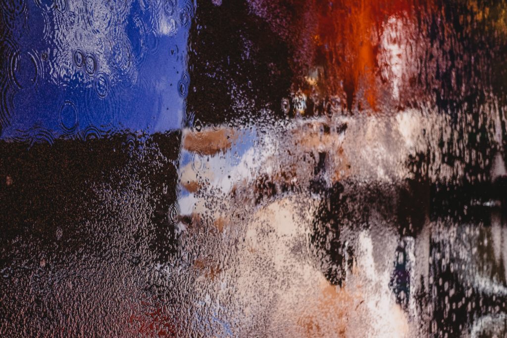 An abstract photo of rain puddles reflected in blue and red light.