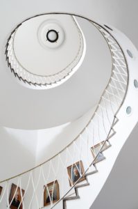 White winding staircase with paintings arranged on the white wall