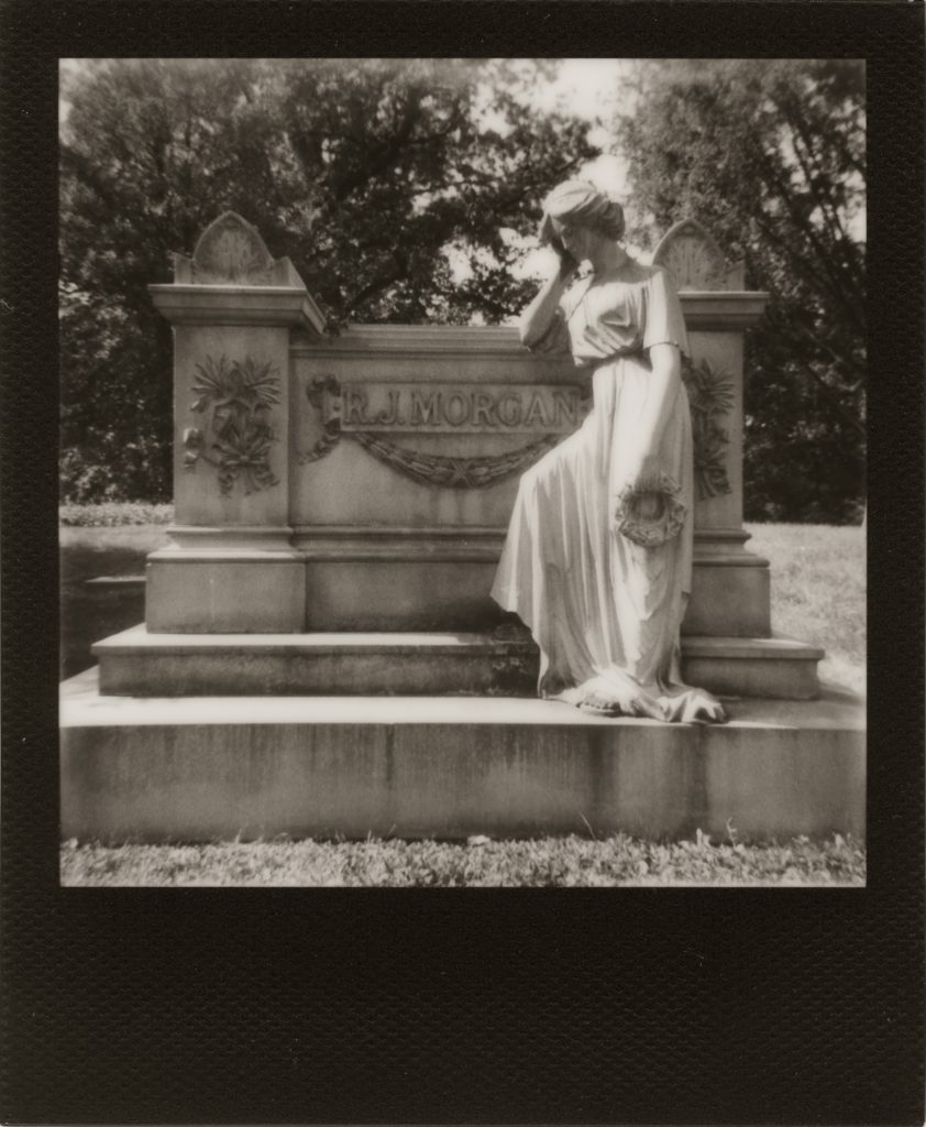 Statue of a female form leaning against a cement stand
