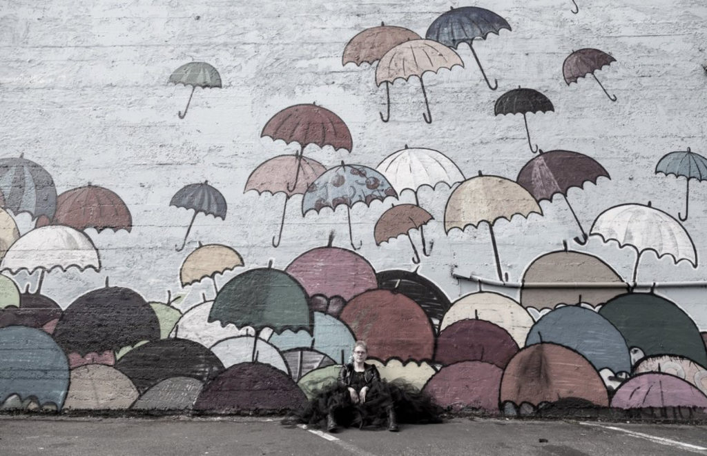 Author photo of Abby Murray. She sits against a mural with an assortment of rainbow umbrellas.