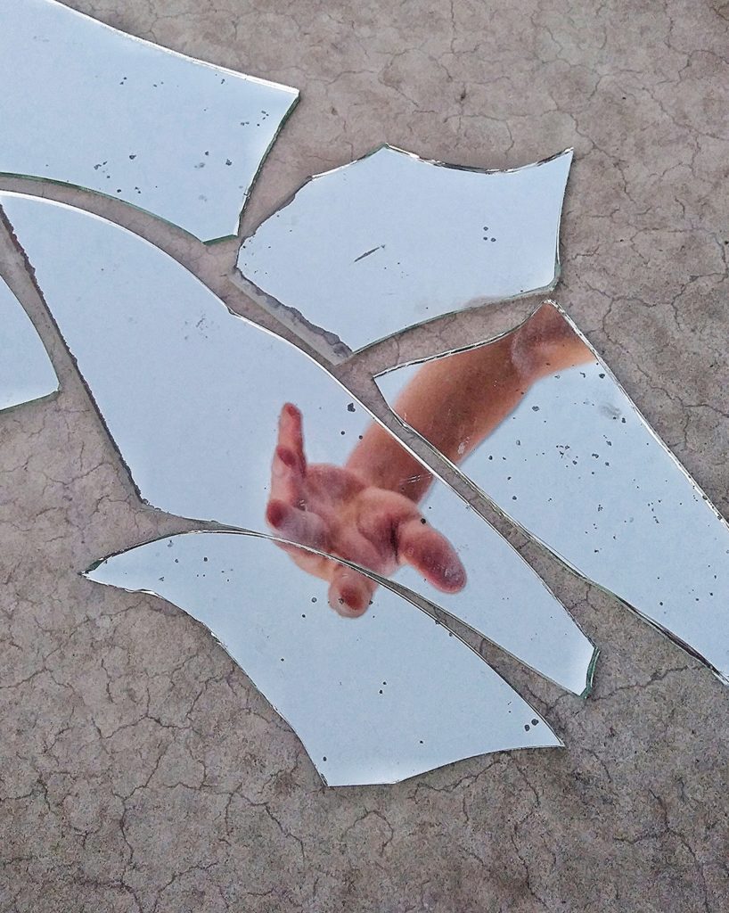 Mirror fragments on the ground depicting an arm