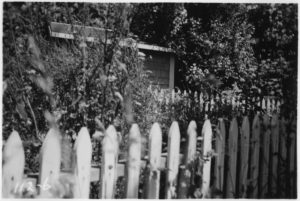 Black-and-white photo of a picket fence around a house