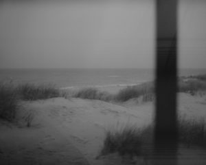 Black-and-white image of a beach as seen through a clear window