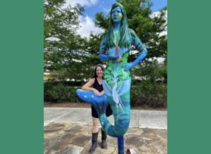 Photo of Jamie Kimmel Shelton standing in front of a large artist rendition of a mermaid