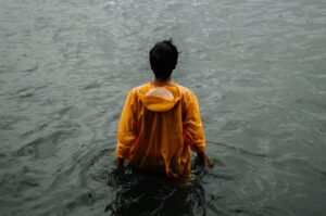 Man in yellow jacket standing in grey water.