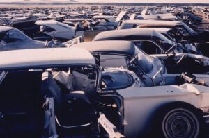 An automobile graveyard. The car in the foreground is missing one of its front doors.