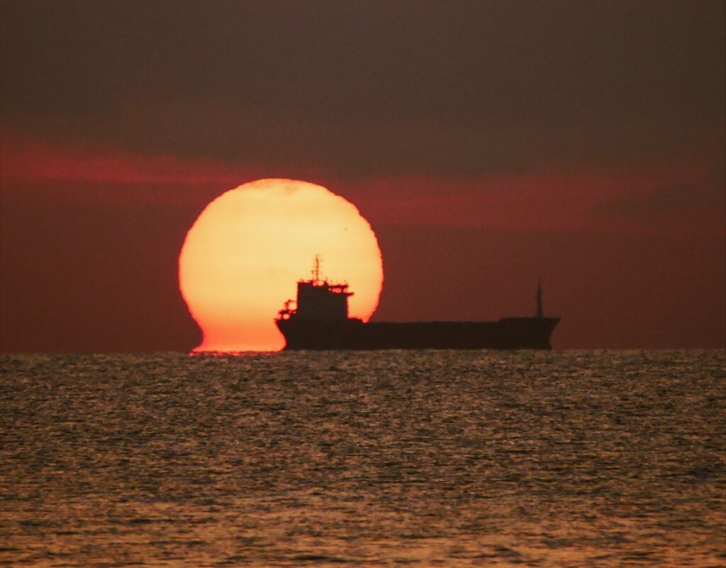 Sun setting on the ocean with the silhouette of a ship visible