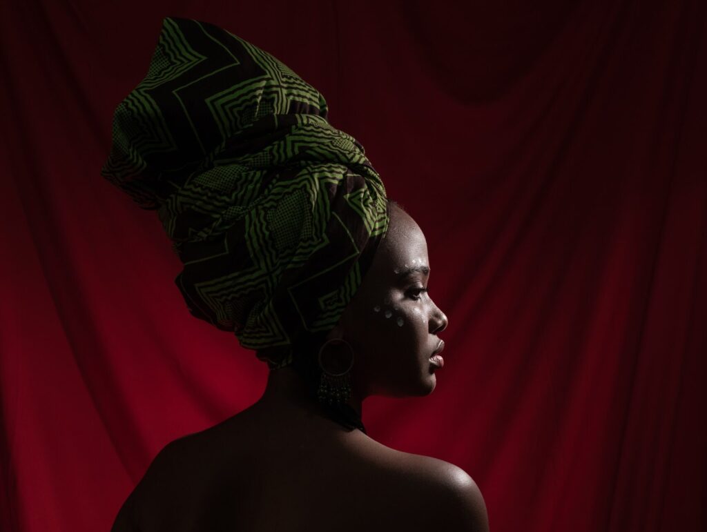 Photo of the back of a black woman in green African clothing against a red background.