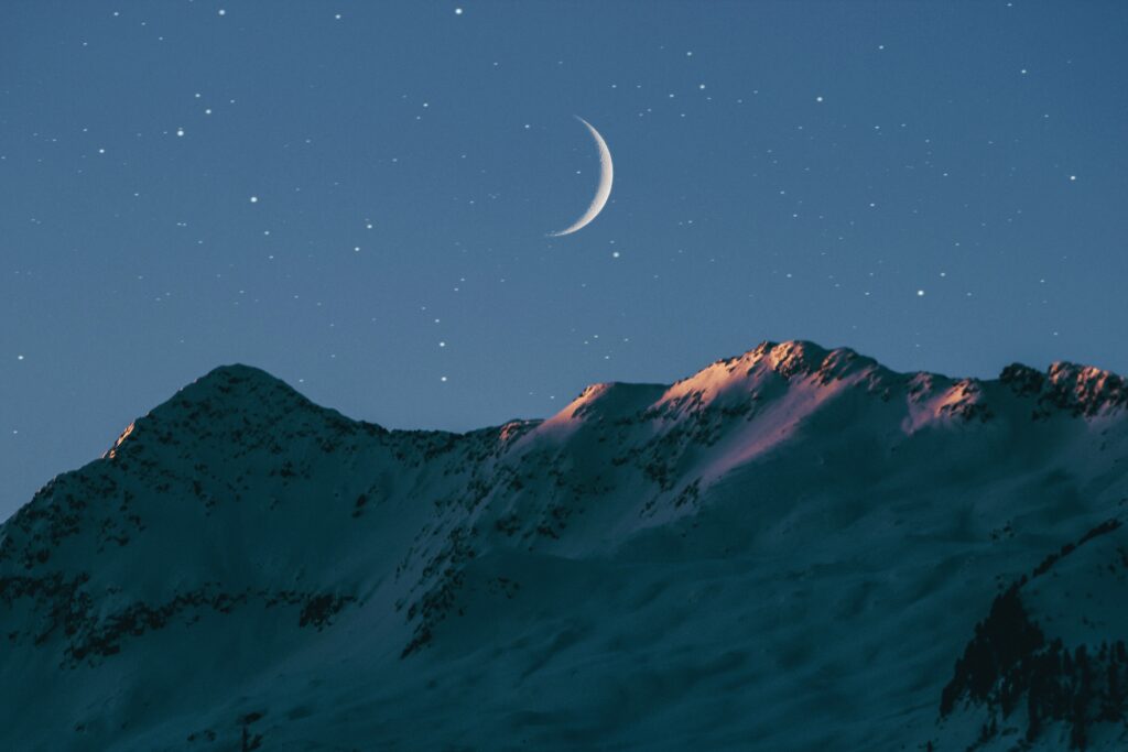 snow capped mountains under night sky with new moon.